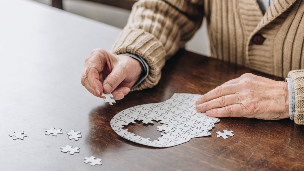 cropped view of senior man playing with a puzzle in the shape of a human head