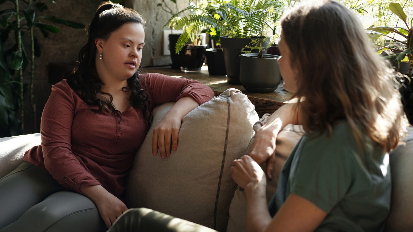 A picture containing a person with down syndrome sitting on sofa with another person